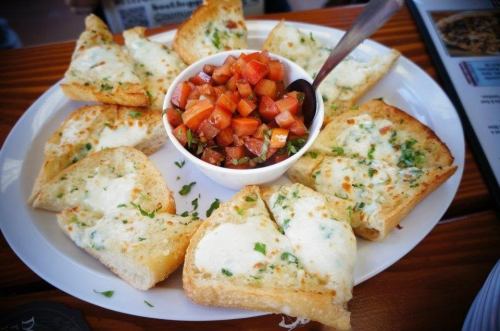 A plate of cheesy garlic bread slices served with a bowl of fresh tomato and olive salsa.
