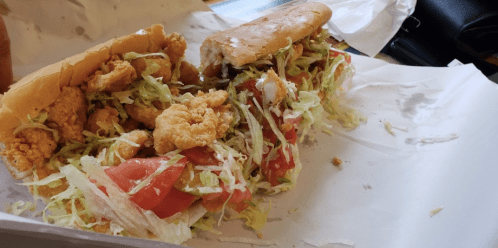 Two sandwiches filled with fried chicken, lettuce, and tomato, served in a paper wrapper.