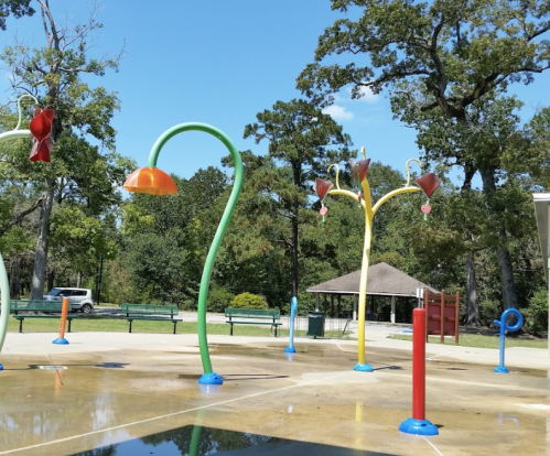 Colorful water play structures in a park, with a blue sky and trees in the background.