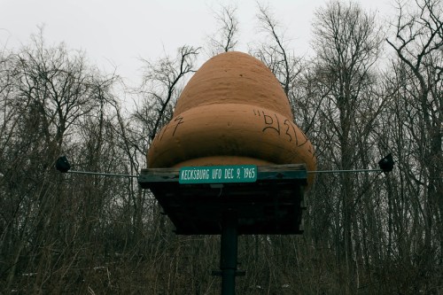 A large, whimsical sculpture resembling a potato sits on a sign marking the Kecksburg UFO incident from December 9, 1965.