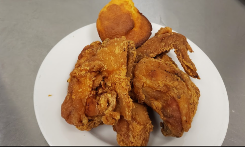 A plate of crispy fried chicken pieces with a golden cornbread muffin on the side.