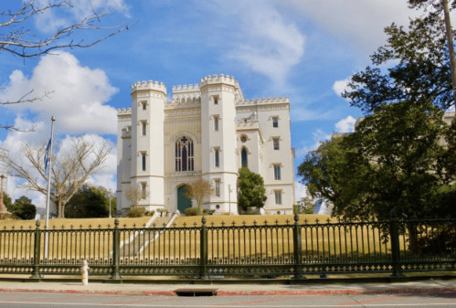 A white castle-like building with turrets, surrounded by greenery and a blue sky with clouds.