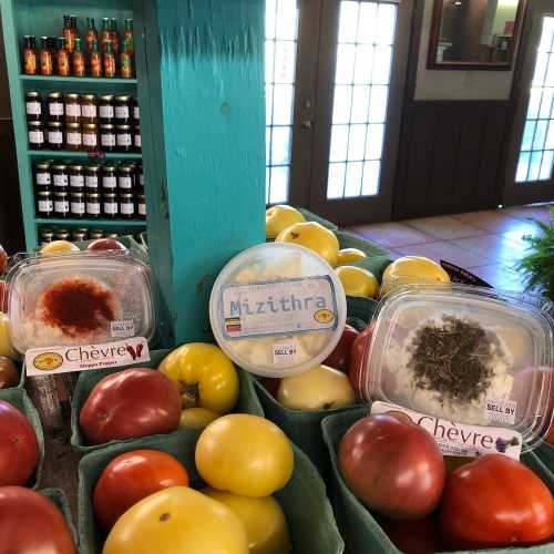 Colorful display of fresh tomatoes and cheese containers at a market, with shelves of jars in the background.