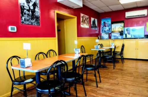 A cozy restaurant interior with red walls, wooden floors, and empty tables set for dining.