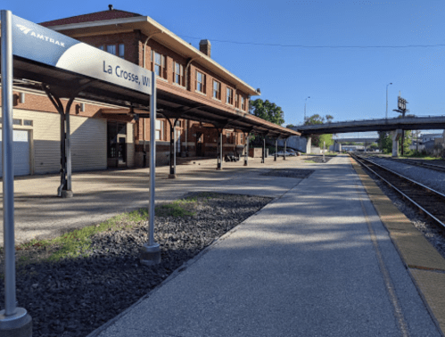 Amtrak station in La Crosse, WI, with a clear sky, empty platform, and nearby train tracks.
