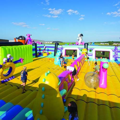 A colorful inflatable playground with children playing and climbing on various structures under a blue sky.