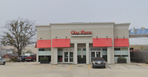Exterior of Chez Pierre French Bakery & Café, featuring red awnings and a modern design, set in a foggy environment.