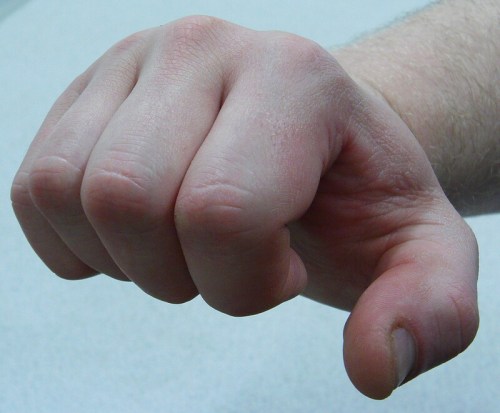 A close-up of a clenched fist with light skin tone against a neutral background.