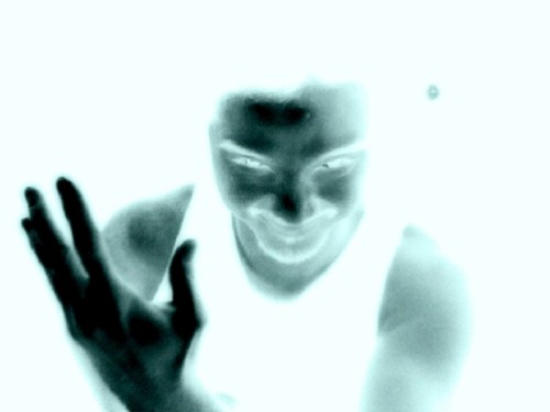 A person with a sinister expression, hands raised, depicted in a negative color effect.