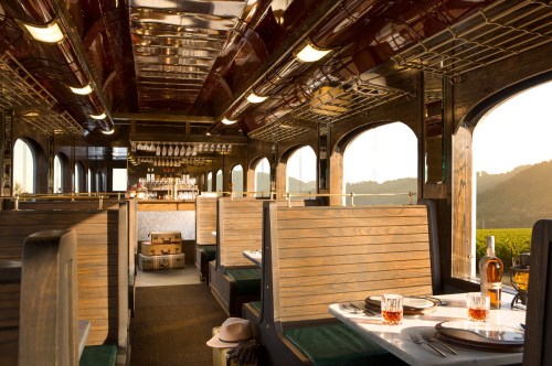 Interior of a vintage train dining car with wooden booths, elegant decor, and scenic views through large windows.