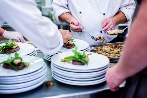 Chefs plating gourmet dishes with vegetables in a busy kitchen setting.