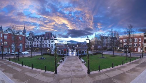 A panoramic view of a charming town square at dusk, featuring historic buildings and a colorful sky.