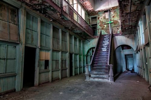 Abandoned interior of a building with peeling paint, a staircase, and empty doorways, evoking a sense of decay.