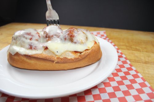 A meatball sub topped with melted cheese, served on a white plate with a fork ready to dig in.