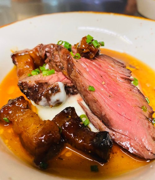 A plate of sliced beef with a glossy sauce, garnished with green onions, served alongside caramelized pieces.