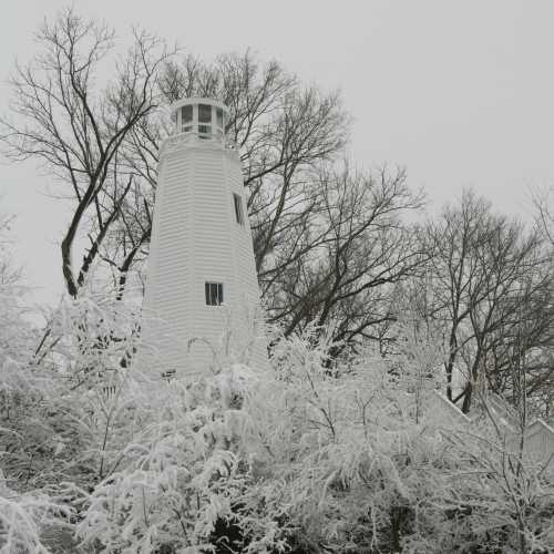 A white lighthouse surrounded by snow-covered trees under a gray sky.