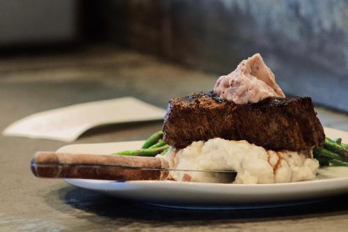 A plate featuring a steak on mashed potatoes, topped with a dollop of sauce, and served with green beans.