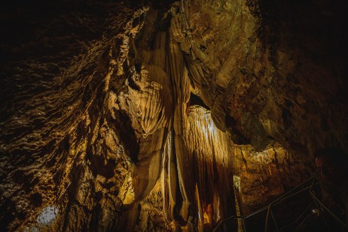 Stalactites and rock formations illuminated in a dark cave, showcasing intricate textures and natural beauty.