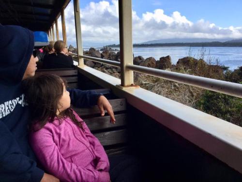A child and an adult sit together on a boat, gazing out at the water and clouds in the distance.