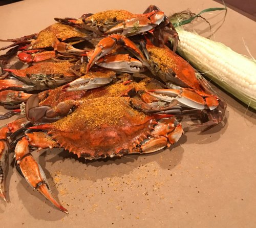 A pile of seasoned crabs on brown paper, next to a cob of corn.