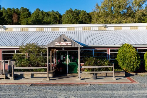 A rustic building with a sign reading "Red Roost," surrounded by greenery and a gravel path.