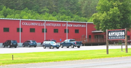 Red building with "Collinsville Antiques of New Hartford" sign, surrounded by green trees and parked cars in front.