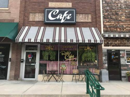 A cozy café with a striped awning, outdoor seating, and large windows displaying a welcoming atmosphere.