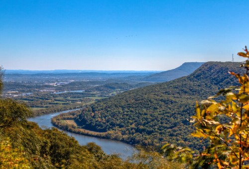 A scenic view of a winding river surrounded by lush green hills under a clear blue sky.