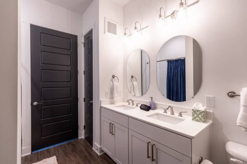 Modern bathroom featuring dual sinks, round mirrors, a dark door, and a blue shower curtain.