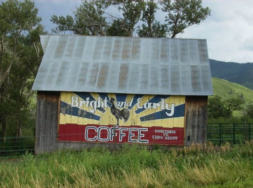 A rustic barn with a colorful sign reading "Bright and Early Coffee" against a scenic green landscape.