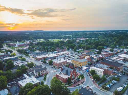 Aerial view of a small town at sunset, featuring streets, buildings, and green fields in the background.