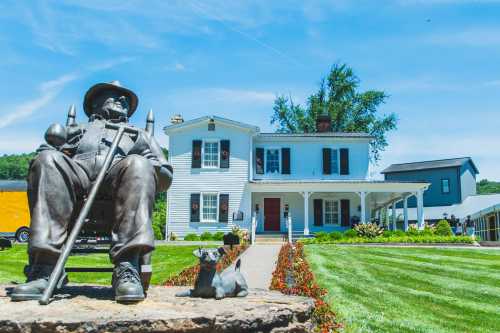 A bronze statue of a man with a dog sits in front of a white house with a porch and well-maintained lawn.