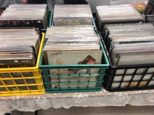 A table with several crates filled with vinyl records, some covered in plastic sleeves.