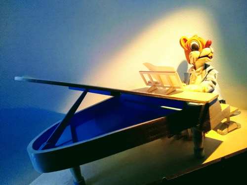 A whimsical figure in a bear costume plays a miniature piano under soft lighting.