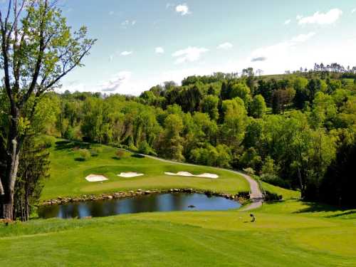 A scenic golf course with lush green hills, a pond, and sand traps under a clear blue sky.