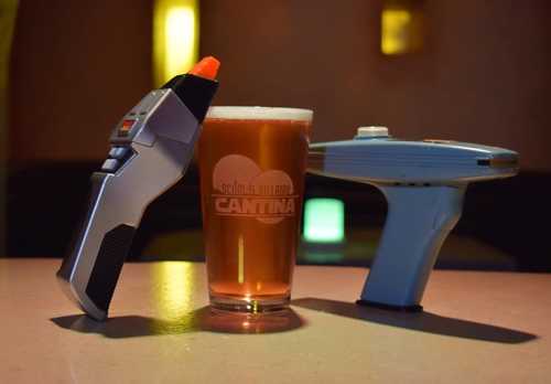 A sci-fi themed drink setup featuring a pint of beer between a futuristic blaster and a communicator device.