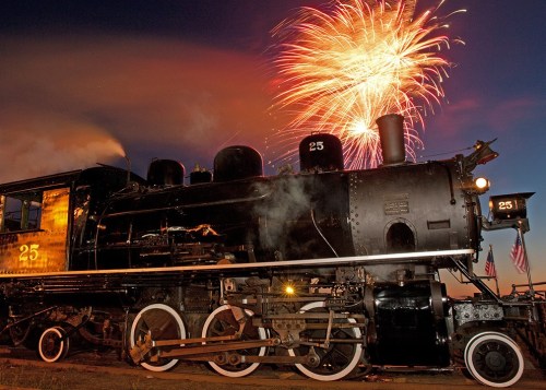 A vintage steam locomotive with fireworks in the night sky, creating a festive atmosphere.