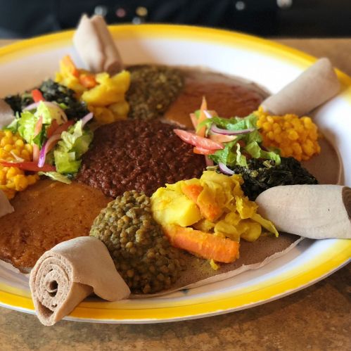 A colorful platter of Ethiopian injera topped with various lentils, vegetables, and salads, arranged artistically.