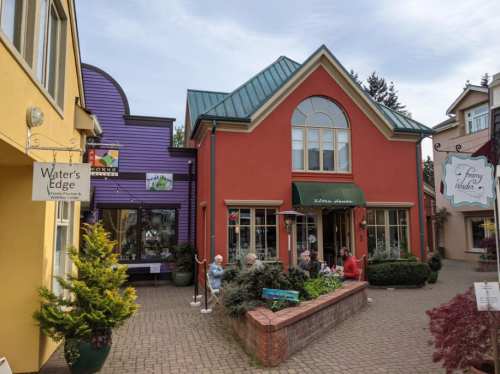 Colorful buildings with a café patio, surrounded by greenery and shops in a charming outdoor setting.