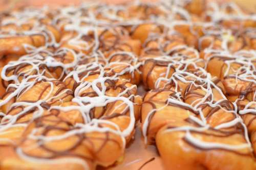 A close-up of glazed donuts drizzled with chocolate and white icing, arranged in a colorful display.