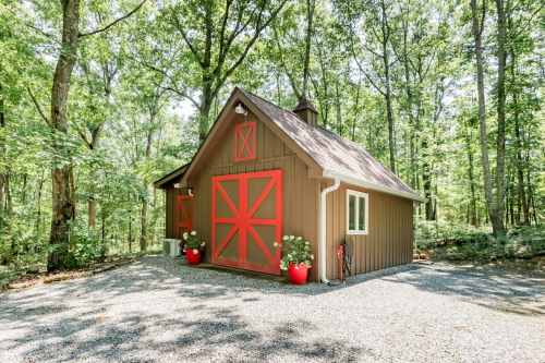 A brown barn-style building with red doors, surrounded by trees and gravel, featuring potted plants at the entrance.
