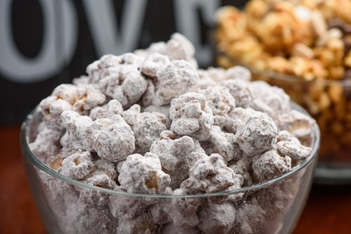 A close-up of a glass bowl filled with powdered sugar-coated popcorn, with another bowl of popcorn in the background.