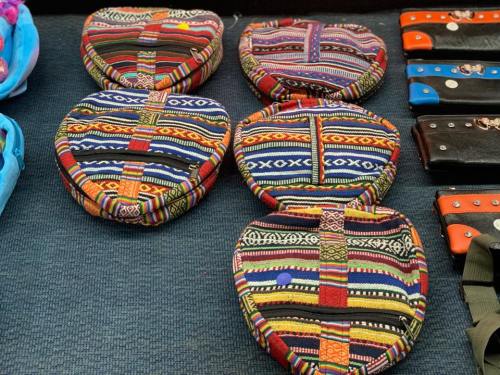 Colorful, patterned round bags displayed on a table, alongside a few leather items.