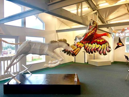 A gallery featuring a large horse sculpture and a colorful bird installation, with bright walls and natural light.