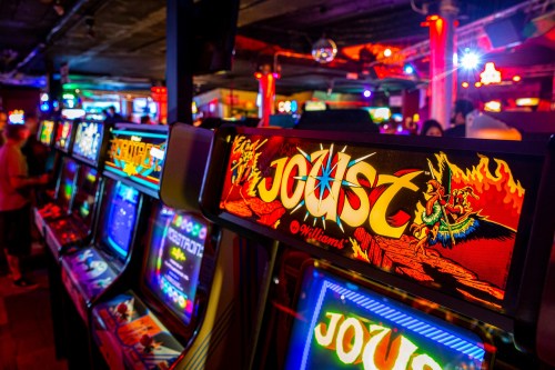 Colorful arcade machines featuring the game "Joust" in a vibrant gaming venue with neon lights.