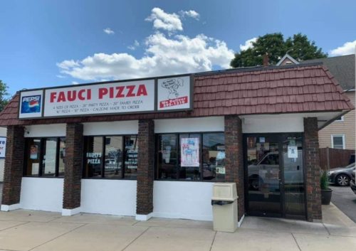 Exterior of Fauci Pizza restaurant with a sign displaying menu options and a clear blue sky in the background.