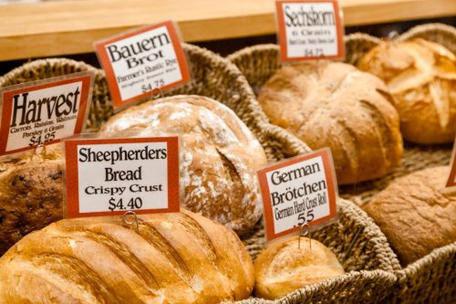 A display of various breads in baskets, each labeled with names and prices, including Sheepherders Bread and German Brötchen.