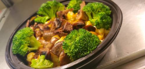 A bowl of sautéed vegetables, including broccoli, mushrooms, and corn, served in a black container.