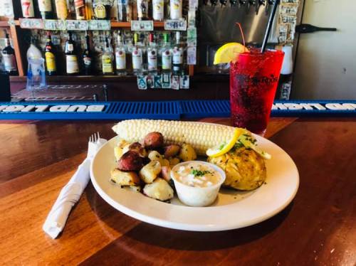 A plate of seafood with corn, potatoes, and a drink with a lemon slice on a bar counter.