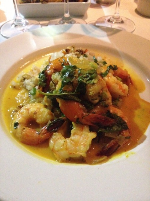 A plate of shrimp sautéed with greens in a yellow sauce, served over a bed of rice or grain.